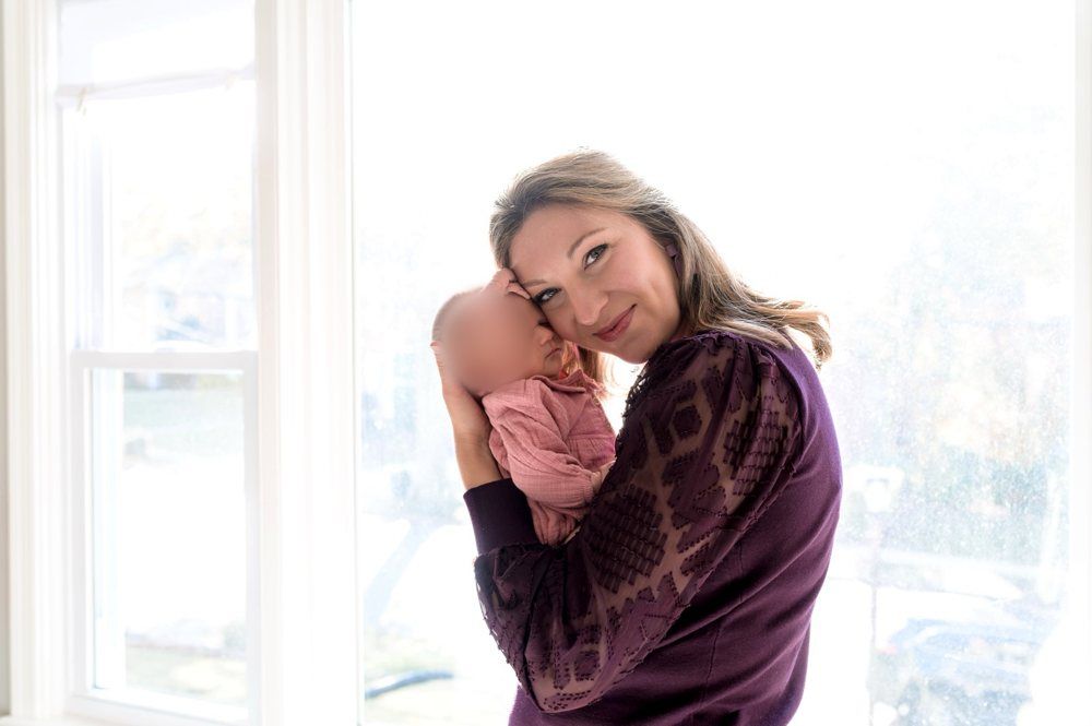 Katelyn holding her newborn daughter by a window